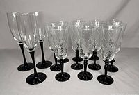 Front angle view showing 11 swirl design glasses with black stems and 3 traditional champagne flutes with black stems arranged in rows.
