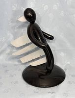 Front side view of the black plastic voodoo doll shaped knife block with four white plastic knives pierced through the torso, standing on a round base.
