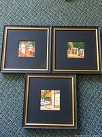 Three black-and-gold framed oil paintings arranged on carpet