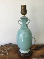 Front view of antique Chinese celadon ceramic vase converted to table lamp mounted on a wooden base, showing rounded body and lamp socket.