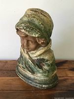 Front view of the antique pottery bust showing the woman's face and detailed shawl with greenish glaze and red accents.