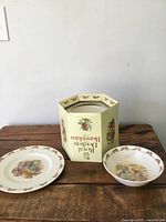 Photo of the full lot arranged on a wooden surface showing the plate, shallow bowl, mug, and original packaging box with Royal Doulton Bunnykins branding and bunny illustrations.