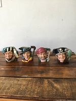 Four Royal Doulton Toby jugs arranged in a row on a wooden surface showing full character faces and handles.