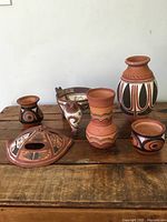 Group shot of all six hand-painted ceramic pottery pieces arranged on wooden table showing color and design variety.