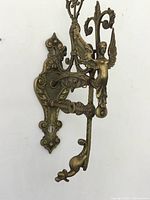 Side view of large antique brass wall sconce with ornamental winged griffin figure and scroll detail