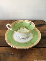 Tea cup and two saucers showing the green and gold ornate design and condition.