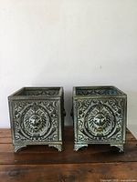 Front view of both planter pots side by side showing embossed lion heads and ornate scrollwork details.