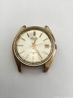 Front view of vintage Seiko watch showing cream dial with gold-tone markers and hands, date display, scratches and surface wear visible on watch face.