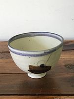 Side view of small artisan pottery tea cup showing cream color with blue-gray rim and brown brushstroke decoration