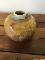 Small vintage Asian ceramic squat vase with rounded shape, floral decoration, and earthy glaze colors.