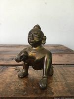 Front angle of small bronze figure sculpture showing detailed facial features and crouching stance on wooden surface.