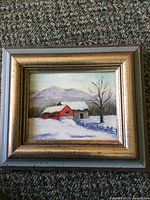 Frontal view of the framed small vintage oil painting showing the winter scene with red barn, snow, tree, and mountains