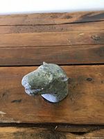 Small soapstone animal head sculpture shown from an angled top view laying on a wooden surface, highlighting the carved features and surface texture.
