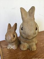 Front view of two ceramic bunny figurines of different sizes on wood surface against white wall.