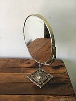 Front view of vintage brass swivel dresser mirror showing oval mirror on decorative base with wear