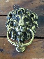 Front view showing detailed lion's head and ring in mouth mounted on wooden background.