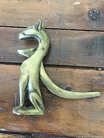 Side view of vintage brass dog-shaped nut cracker showing the full figure and tail, surface wear visible.