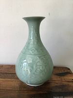Front view of vintage Chinese celadon ceramic vase with pear-shaped body and flared neck on wooden surface.