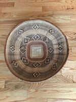 Top down photo of a round woven basket with geometric diamond pattern and square center, placed on a wooden floor.