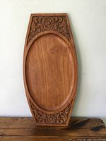 Full view of the front of the teak serving tray showing carved floral details on both ends and oval recessed center.