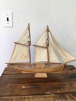 Front angled view of vintage wooden model ship with two masts, cloth sails stained and discolored, mounted on wooden stand.