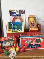 Full lot of vintage toys displayed on a white background including magnet set, take apart toy, peg doll, whistle, and boxed balance scale