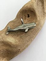Front view of vintage whale pendant on wooden surface showing overall shape, silver-toned with tarnish and wear.