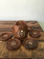Wooden coaster set arranged around the wooden holder on a wooden surface showing design details and condition.