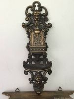 Full view of antique cast iron wall sconce, showing ornate design with faces and scrollwork.
