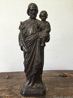 Front view of the antique cast spelter religious statue showing the robed male figure holding a child with detailed folds in the robe.