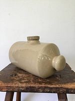 Side and top view of the antique cream-colored ceramic water bottle with stopper, showing its rounded rectangular shape and glaze.