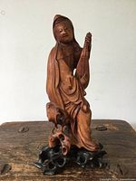 Front-left angled view of the carved boxwood figure on its root wood stand showing the figure holding a musical instrument.