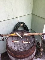 Wooden ox yoke with multiple vintage fishing lures displayed on it, sitting on a wooden barrel against a wall.