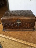 Front view of the antique leather sewing box showing embossed cherubs, grapes design and brass hardware clasp on a wooden surface.