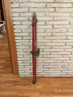 Full view of the red painted antique ox yoke against a white brick wall, showing its full length and wear.