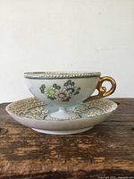 Side view of porcelain tea cup showing hand painted flowers, gold handle and embossed rims
