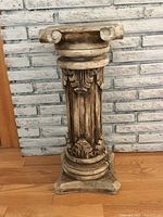 Full frontal view of the antique wood carved column standing against a brick wall on a wooden floor.