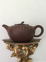 Side view of reddish-brown Yixing clay teapot with round body, curved spout, circular handle, and signature on lid base.