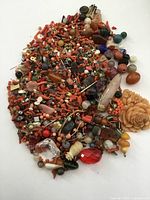 Top view of a mixed group of crafting beads of various shapes, sizes, and colors, predominantly coral and amber tones with other assorted beads and components scattered throughout.