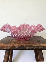 Side view of the cranberry glass bowl showing hobnail texture and deep ruffled edge with white opalescent accents.