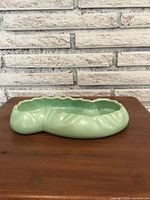 Side view of light green decorative ceramic dish with kidney bean shape on wooden surface against a white brick wall background.