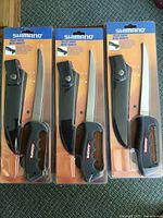 Front angle showing three packaged Shimano fillet knives with sheaths, black handles with red/white Shimano branding.