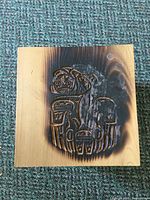 Top view of the cedar box lid showing the burnt surface around an Indigenous carved design.