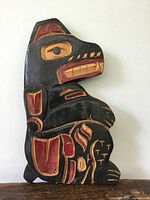 Front view of the carved wooden bear figure showing black, red, and yellow paint with Indigenous design.