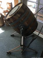Side view of wooden barrel butter churn on metal stand with crank handle and metal bands.