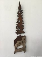 Full view of the saw carving wall decor featuring a tree-shaped rusty metal blade and wooden handle with hooks.