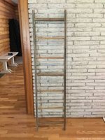 Full view of the rustic wooden ladder standing vertically against a whitewashed brick wall showing its overall size and shape.