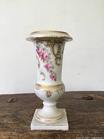 Full frontal view of the antique Sevres porcelain vase showing floral and gold painted details against white porcelain, standing on a wooden surface.