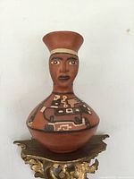 Front view of the antique southern pottery jug showing the hand-painted human face and geometric designs on reddish-brown terracotta.