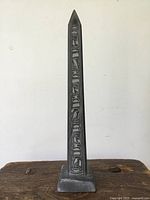 Front view of the vintage stone obelisk showing carved designs on one side.